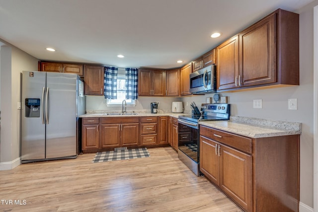 kitchen with recessed lighting, stainless steel appliances, a sink, light wood-type flooring, and brown cabinets