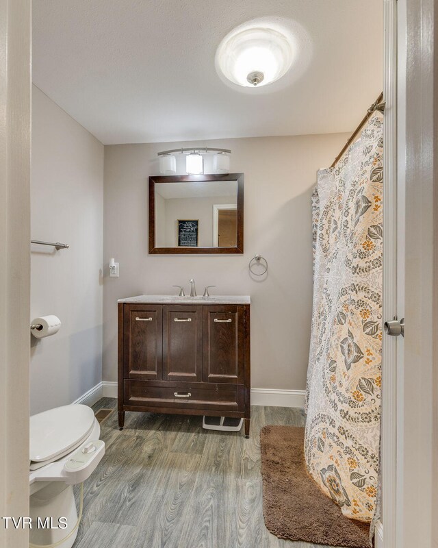 full bathroom with toilet, wood finished floors, vanity, and baseboards