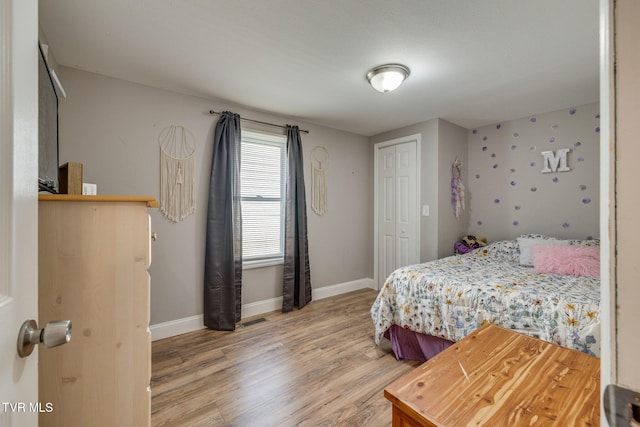 bedroom featuring light wood-type flooring, visible vents, baseboards, and a closet