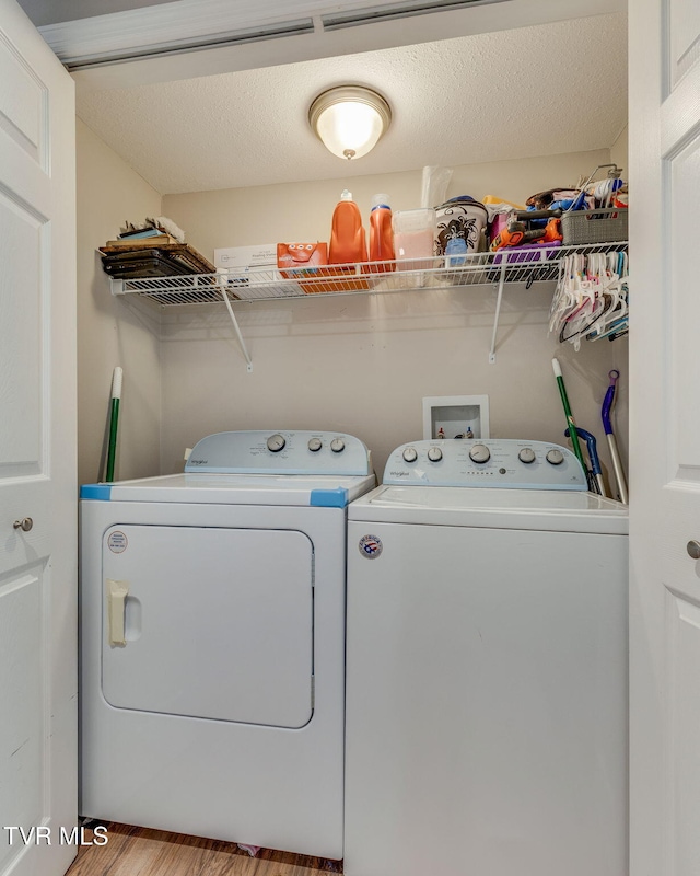 washroom with a textured ceiling, laundry area, separate washer and dryer, and wood finished floors