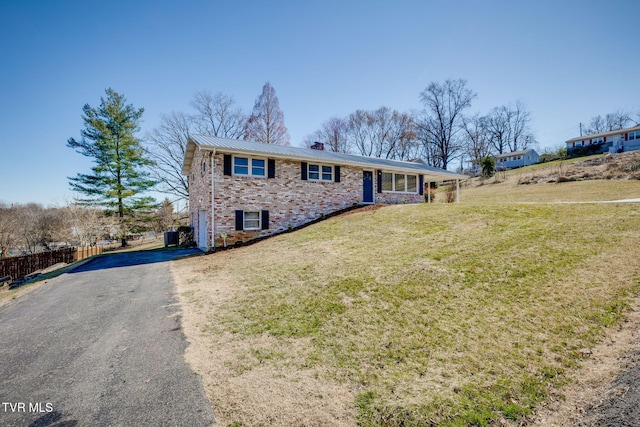 single story home featuring metal roof, aphalt driveway, brick siding, a chimney, and a front yard