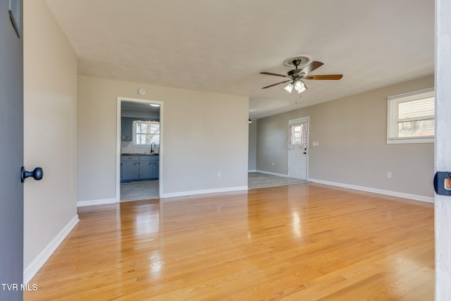 unfurnished room with light wood-type flooring, a sink, a ceiling fan, and baseboards