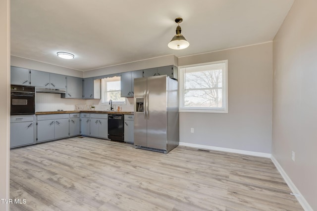 kitchen with under cabinet range hood, a sink, gray cabinets, black appliances, and light wood finished floors