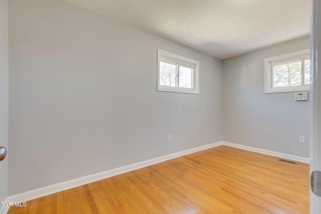 unfurnished room with light wood-type flooring, plenty of natural light, visible vents, and baseboards