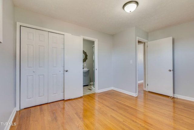 unfurnished bedroom featuring light wood finished floors, connected bathroom, baseboards, and a closet