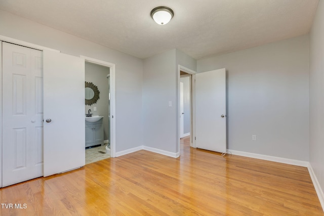 unfurnished bedroom featuring light wood-style floors, a sink, baseboards, and ensuite bathroom