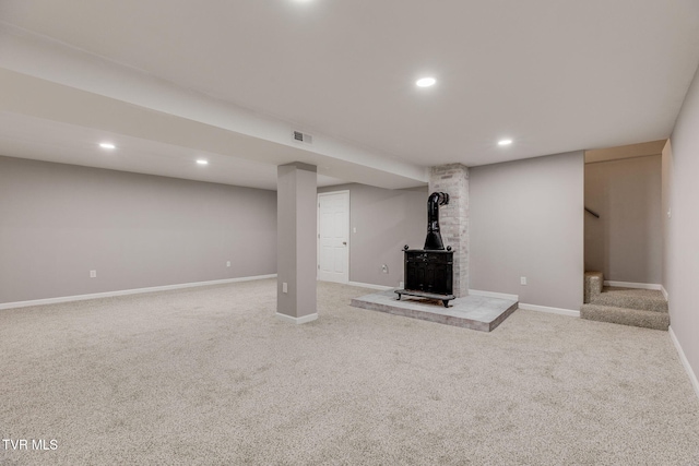 finished basement with a wood stove, stairs, visible vents, and carpet flooring