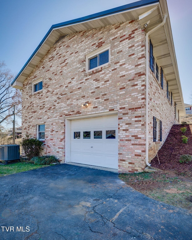 view of property exterior with a garage, brick siding, aphalt driveway, and central AC unit