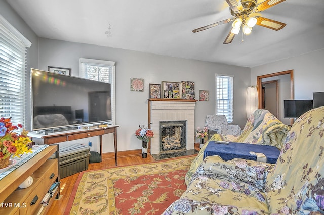 living area with a brick fireplace, wood finished floors, and a ceiling fan