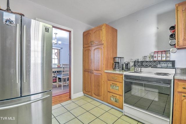 kitchen with light tile patterned floors, electric stove, light countertops, freestanding refrigerator, and brown cabinets