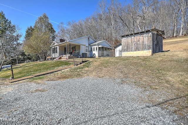 view of front facade featuring a chimney, a detached garage, a porch, an outdoor structure, and a front lawn