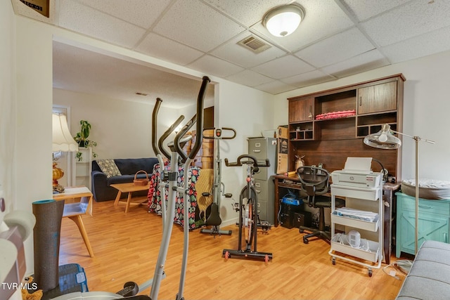 exercise area with light wood finished floors, a drop ceiling, and visible vents