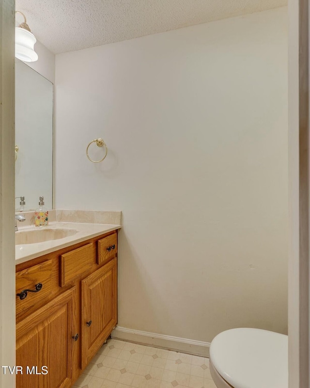 bathroom featuring toilet, a textured ceiling, vanity, baseboards, and tile patterned floors