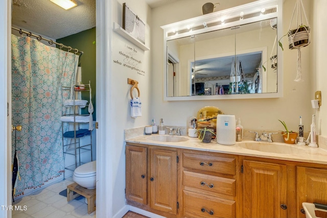 full bathroom with a textured ceiling, double vanity, a sink, and toilet