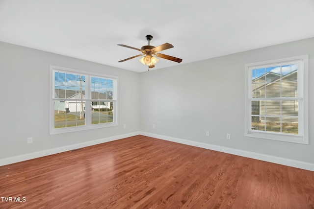 empty room with a wealth of natural light, visible vents, baseboards, and wood finished floors