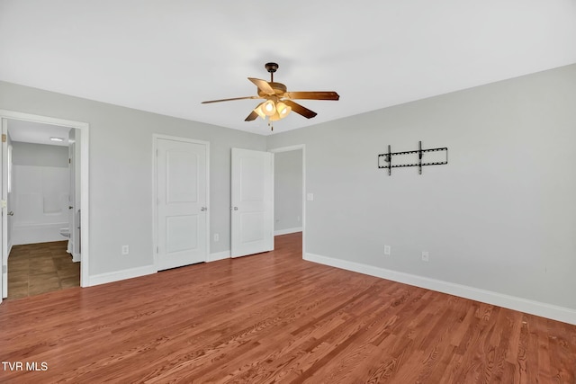 unfurnished bedroom featuring ensuite bathroom, ceiling fan, light wood finished floors, and baseboards