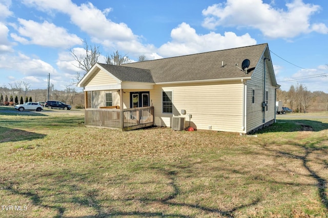 back of property with central air condition unit, a deck, a lawn, and roof with shingles