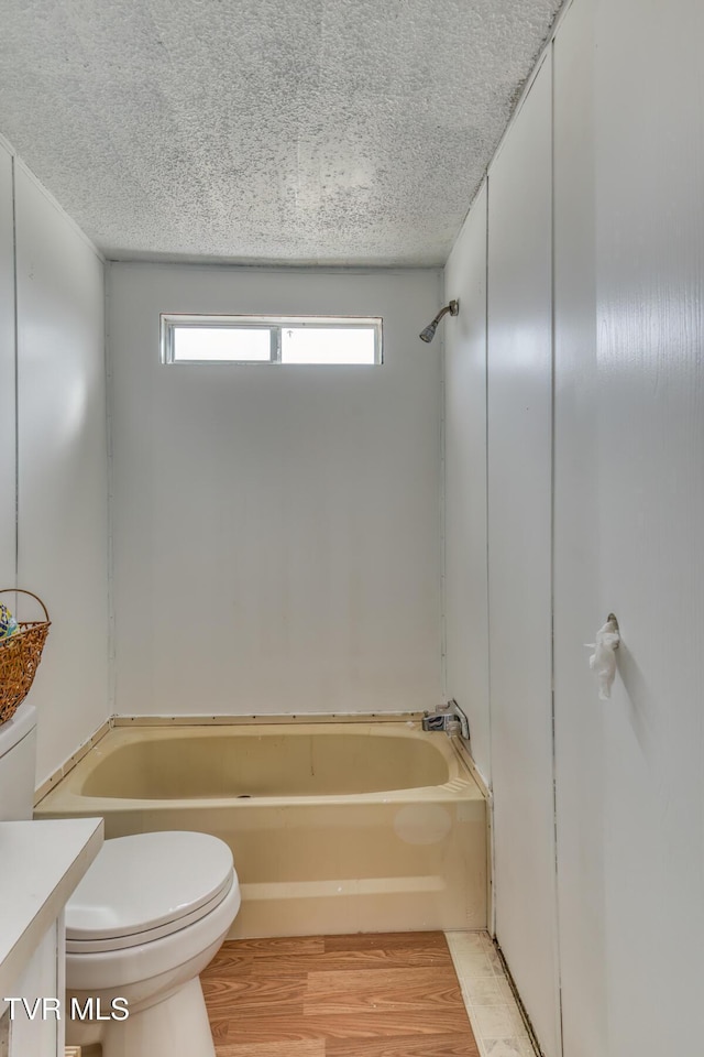 full bath featuring a textured ceiling, toilet, shower / bath combination, wood finished floors, and vanity