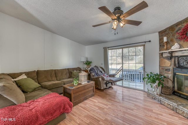 living room with a textured ceiling, a stone fireplace, wood finished floors, and a ceiling fan