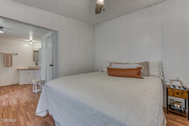 bedroom featuring light wood-style flooring, connected bathroom, ceiling fan, and a sink