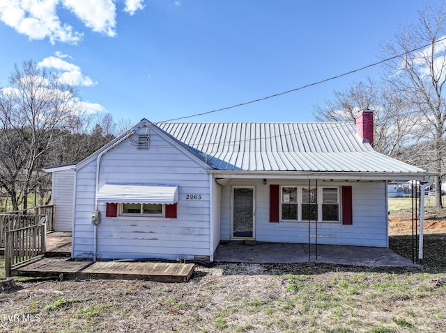 view of front of home with metal roof, a chimney, a deck, and a patio