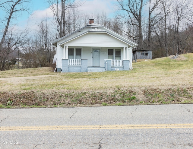 bungalow-style home with covered porch, a chimney, and a front lawn