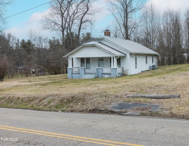 view of front facade with a porch, cooling unit, a front lawn, and a chimney