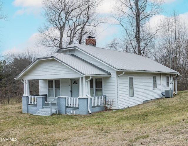 view of front of property with metal roof, a chimney, covered porch, and a front lawn