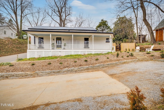 view of front facade with solar panels, a porch, metal roof, and driveway