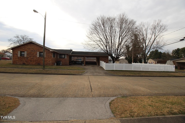 ranch-style home with a carport, concrete driveway, brick siding, and fence