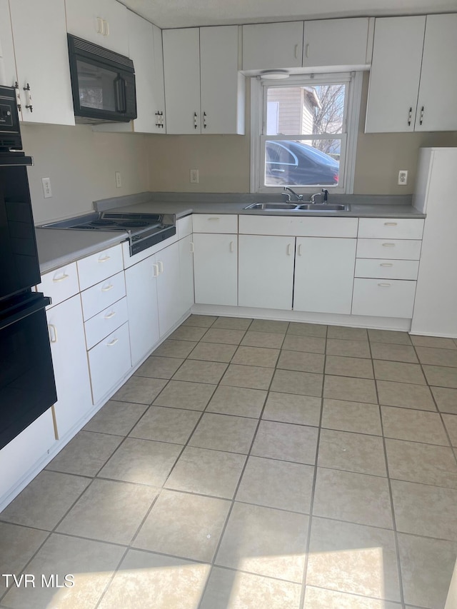 kitchen with light tile patterned floors, a sink, black appliances, white cabinets, and light countertops