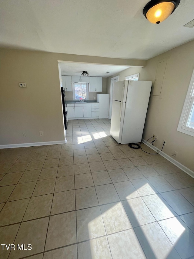 interior space featuring baseboards, light tile patterned floors, freestanding refrigerator, white cabinets, and refrigerator