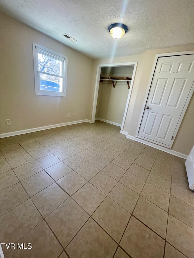 unfurnished bedroom with tile patterned flooring, baseboards, visible vents, and a textured ceiling