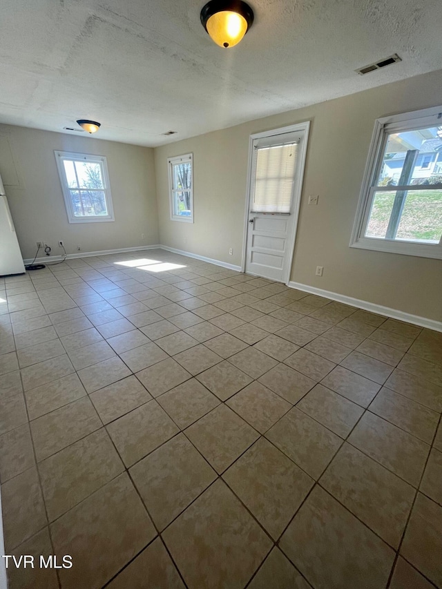 empty room with tile patterned floors, visible vents, a textured ceiling, and baseboards