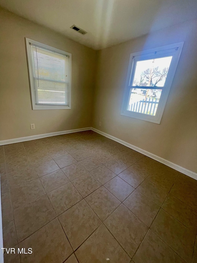 empty room featuring dark tile patterned floors, visible vents, and baseboards