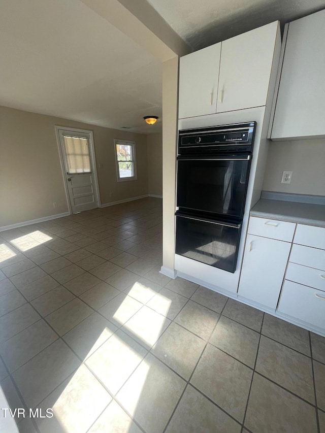 kitchen featuring baseboards, open floor plan, light tile patterned flooring, white cabinetry, and dobule oven black