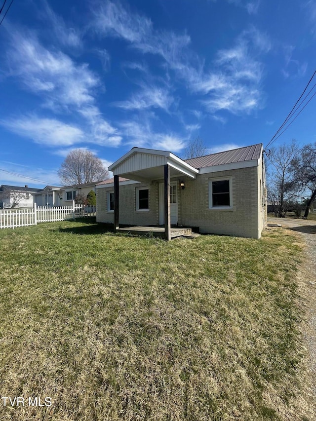 rear view of house with fence, a lawn, and metal roof