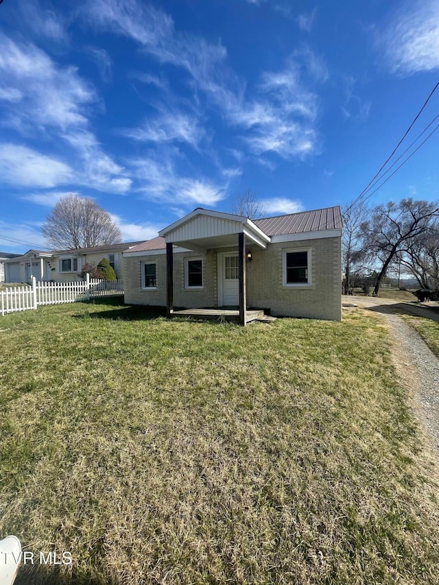 view of front of property featuring metal roof, brick siding, a front lawn, and fence