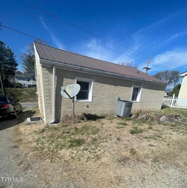 view of property exterior featuring metal roof, brick siding, and fence