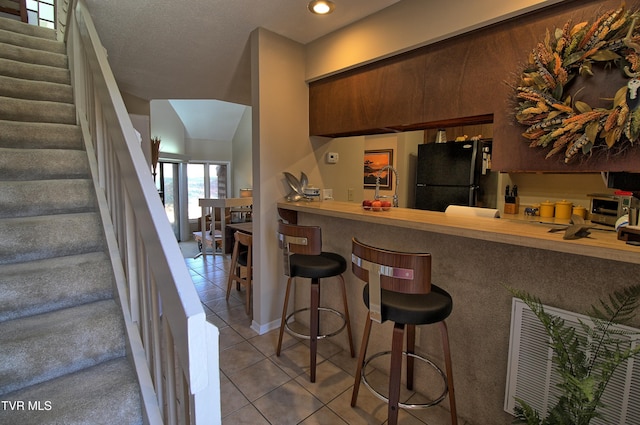 kitchen featuring a breakfast bar, a sink, visible vents, freestanding refrigerator, and tile patterned floors