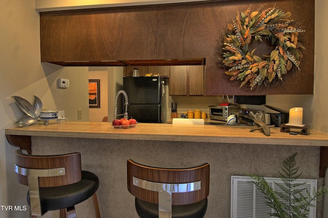 kitchen with a breakfast bar, freestanding refrigerator, a toaster, and a peninsula