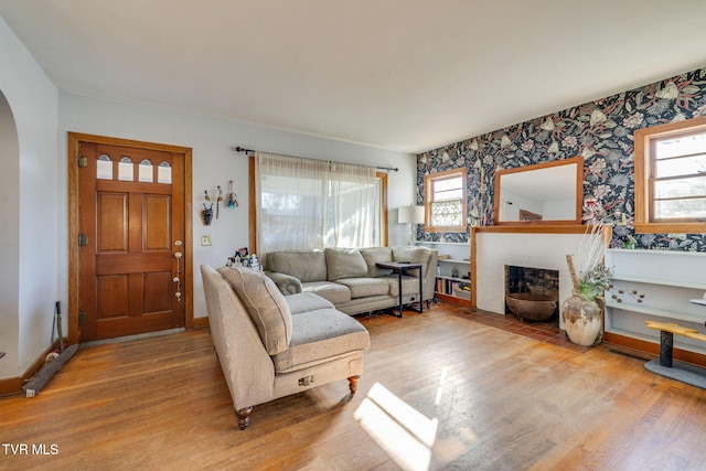 living area with arched walkways, a brick fireplace, baseboards, and wood finished floors