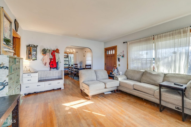 living room featuring arched walkways, light wood-style flooring, and a notable chandelier