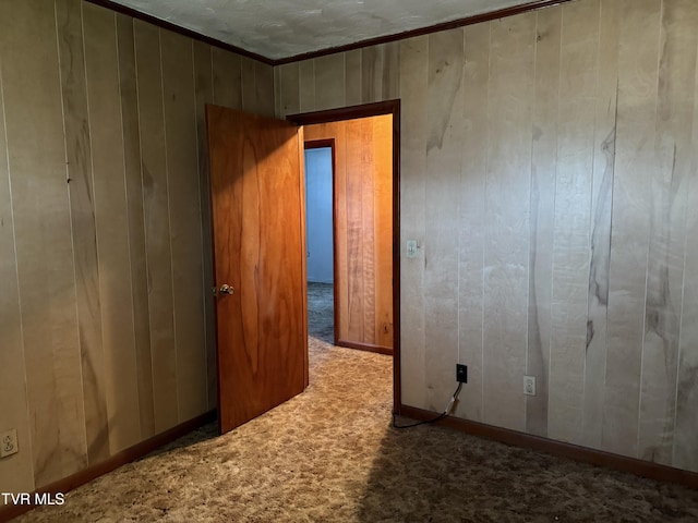 carpeted empty room with ornamental molding and wood walls