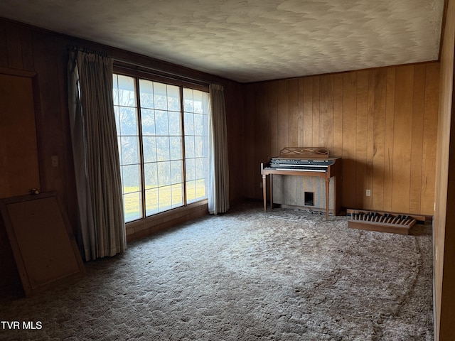 unfurnished living room featuring carpet floors, wooden walls, and a textured ceiling