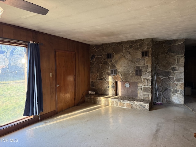 unfurnished living room with a stone fireplace, tile patterned floors, and wooden walls