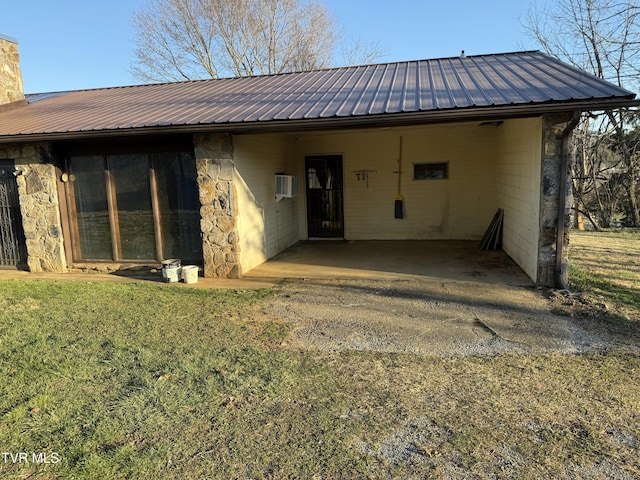 back of house with stone siding, a chimney, metal roof, a yard, and a carport