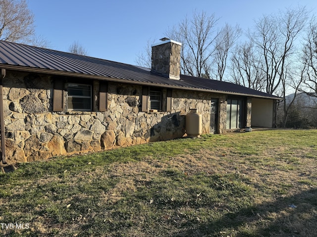 rear view of property featuring a lawn, stone siding, a chimney, metal roof, and a standing seam roof