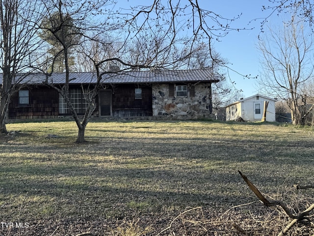 view of front of house featuring metal roof, stone siding, and a front yard