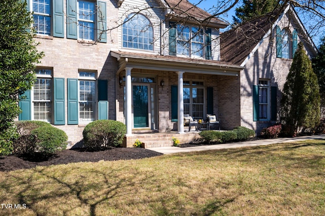 view of front facade featuring covered porch, a front yard, and brick siding